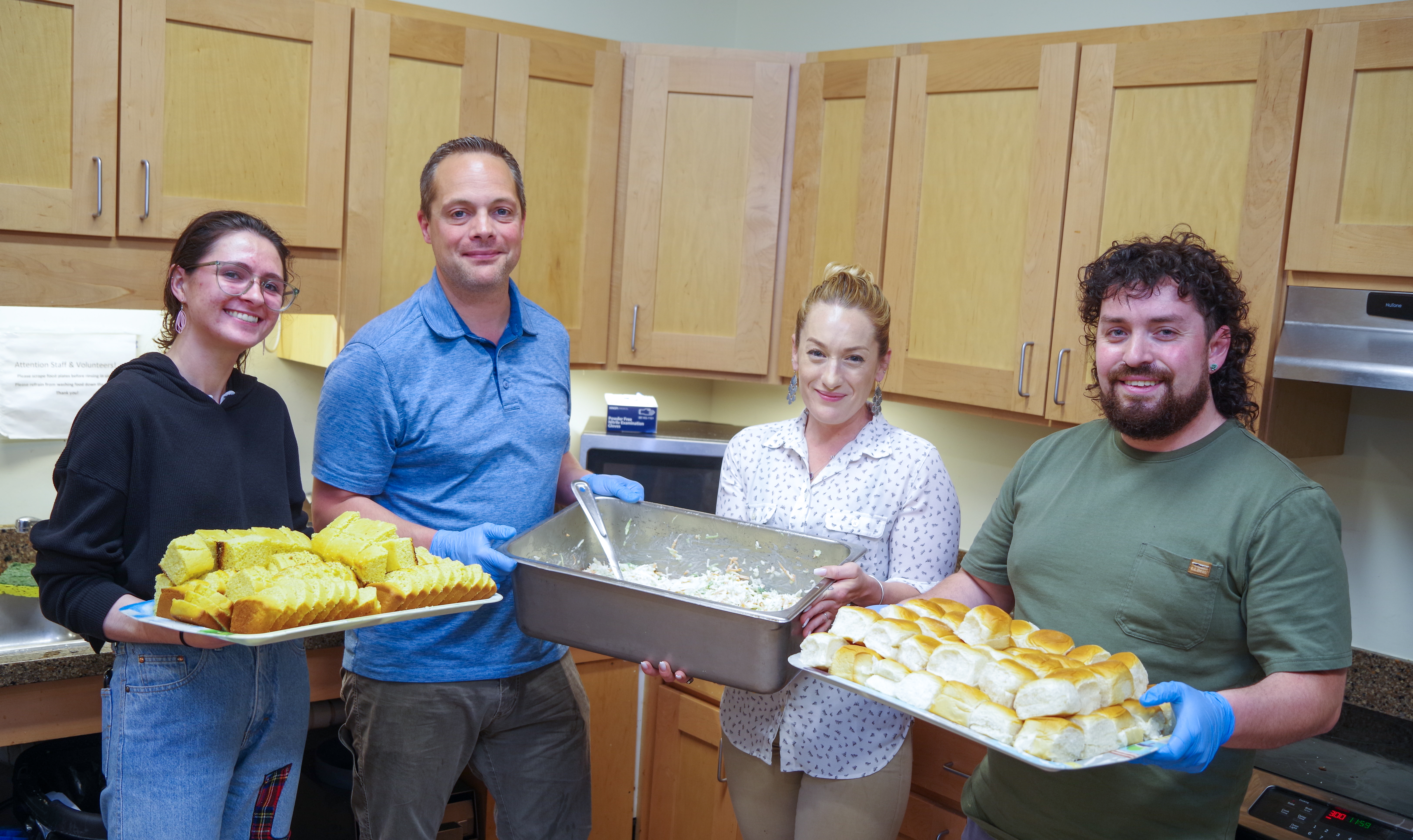 Four COTS volunteers in the shelter kitchen, holding serving trays filled with hot food.
